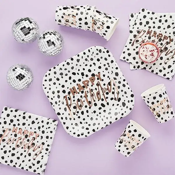 Black and white dalmatian spot party tableware with birthday plates, cups, napkins, and small disco balls on a pastel background